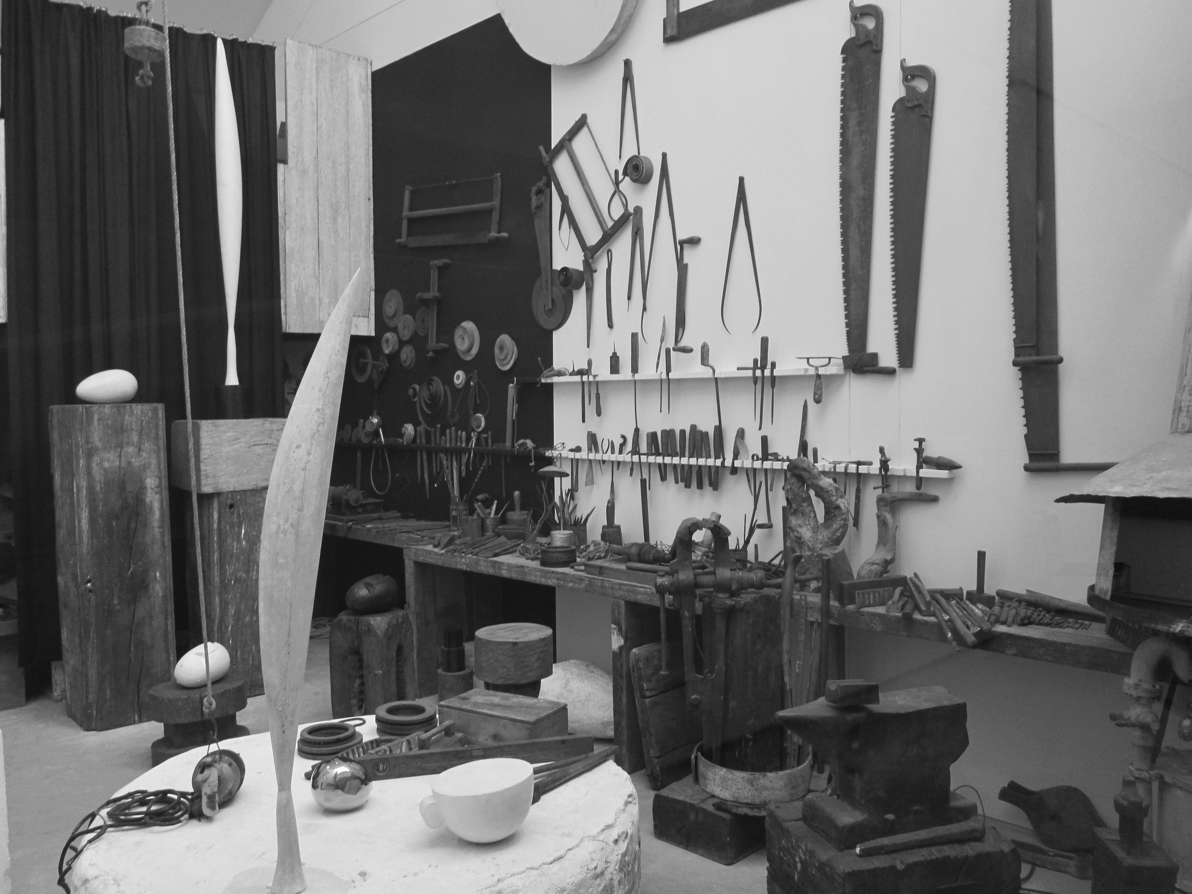 L’atelier de Constantin Brancusi en noir et blanc : scies, compas et ciseaux accrochés au mur au-dessus d’un long établi, sculptures blanches au premier plan