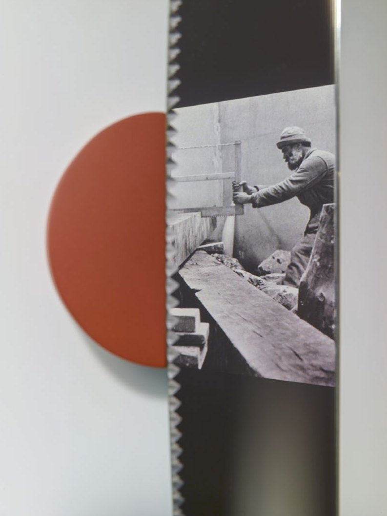 Lame de scie en miroir devant un demi-disque rouge ; on y voit un scieur de long photographié en noir et blanc