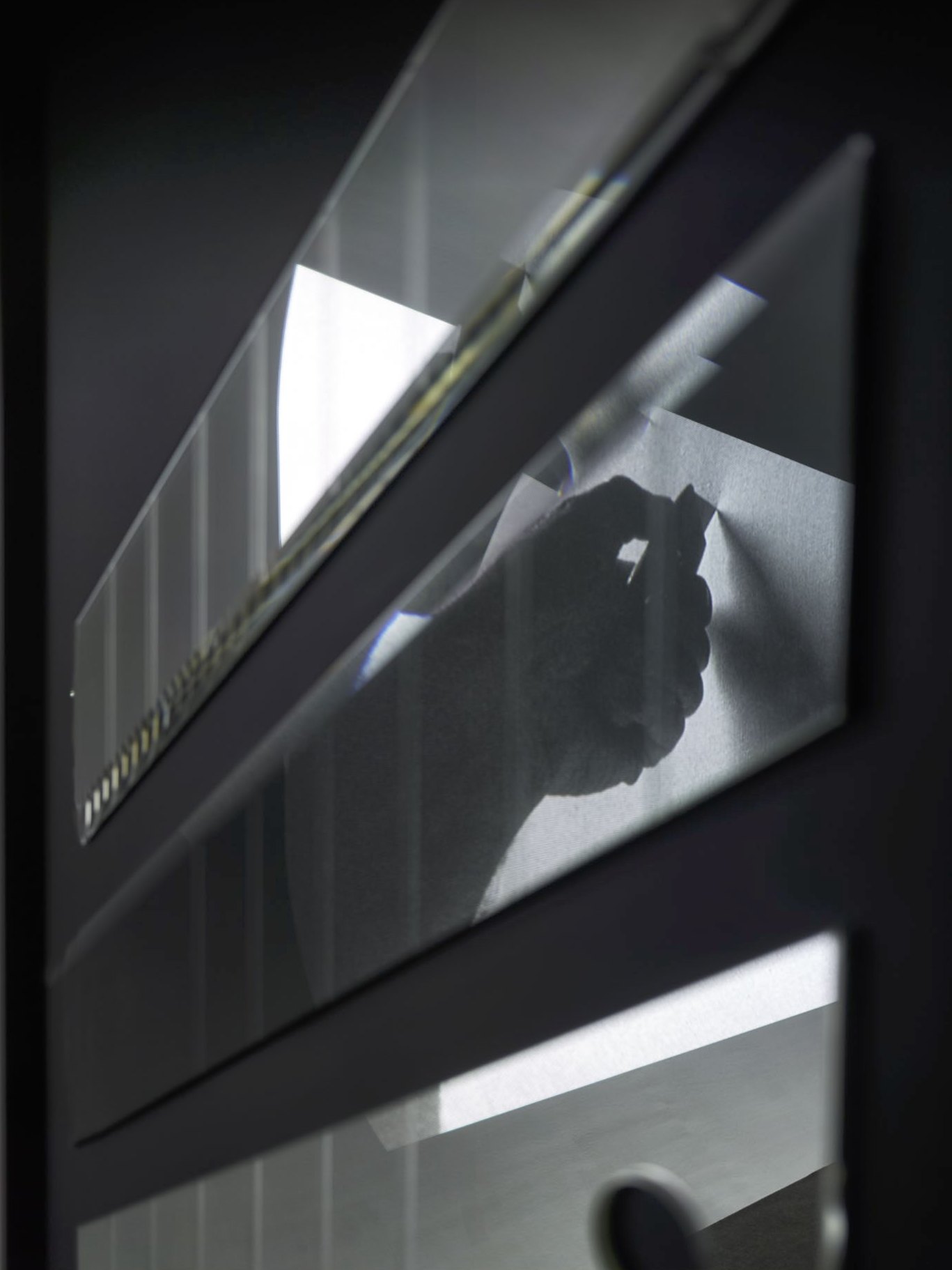Lames de cutter en miroir sur fond noir, vues de biais ; la main de Fontana s’y reflète