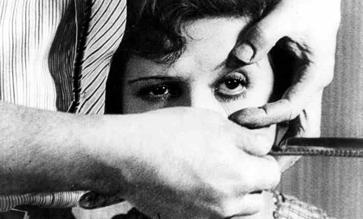 Photogramme noir et blanc : une main écarte l’œil d’une femme, un rasoir approche